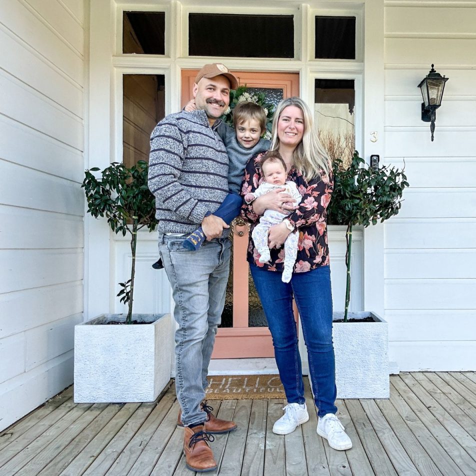 Parents and their two young kids standing in front of the front door of their home.
